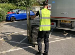 Member of GXO staff wearing high vis GXO top pushing a trolley to the back of a lorry